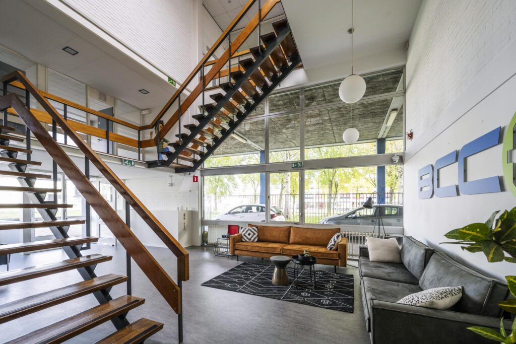 Modern office lobby at Van der Madeweg with wooden staircases, large windows, and comfortable seating area.